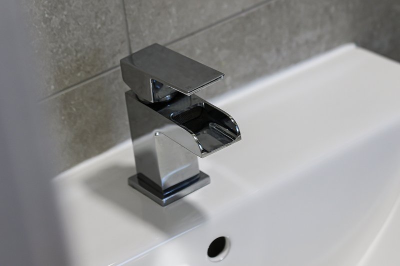 Modern bathroom sink with black waterfall tap and grey tiled wall