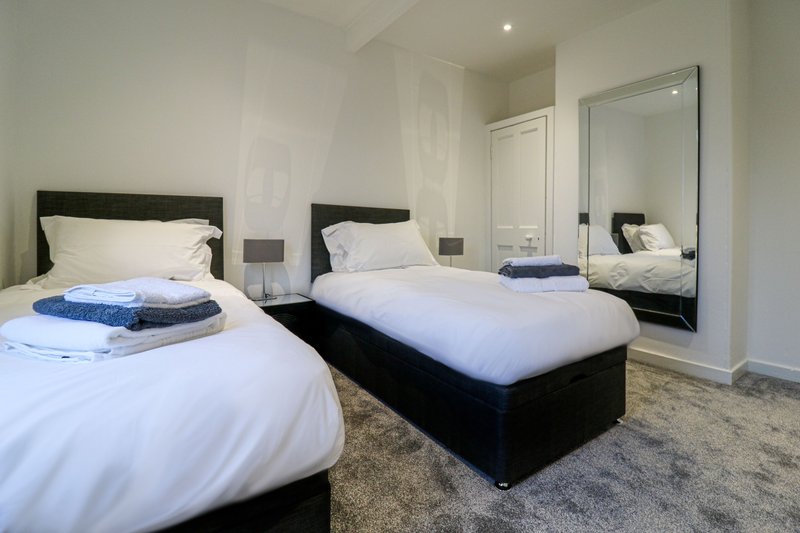 Modern bedroom with two single beds, black frames, white bedding, large mirror and neutral decor