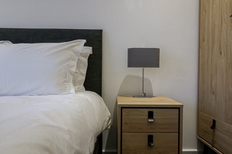 Bedroom with double bed, white bedding, wooden nightstand, and grey lamp