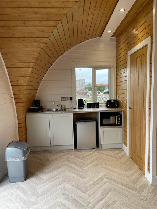 Modern kitchenette with curved white cabinetry, herringbone flooring, wooden ceiling and window view