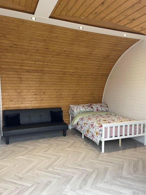 Bedroom with wooden ceiling, black sofa, white single bed with floral bedding, herringbone floor