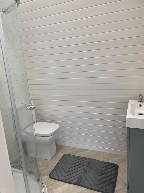 Small bathroom with toilet, shower cubicle, sink and black floor mat