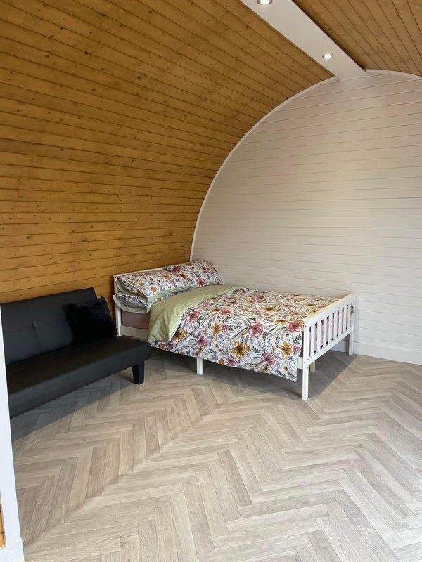 Attic bedroom with wooden ceiling, black sofa, white bed frame, herringbone floor