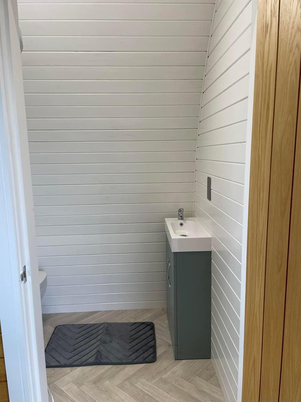 Compact bathroom with white shiplap walls, dark vanity unit, and herringbone floor tile