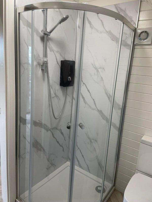 Modern bathroom with curved glass shower enclosure, marble-effect tile walls and chrome fixtures