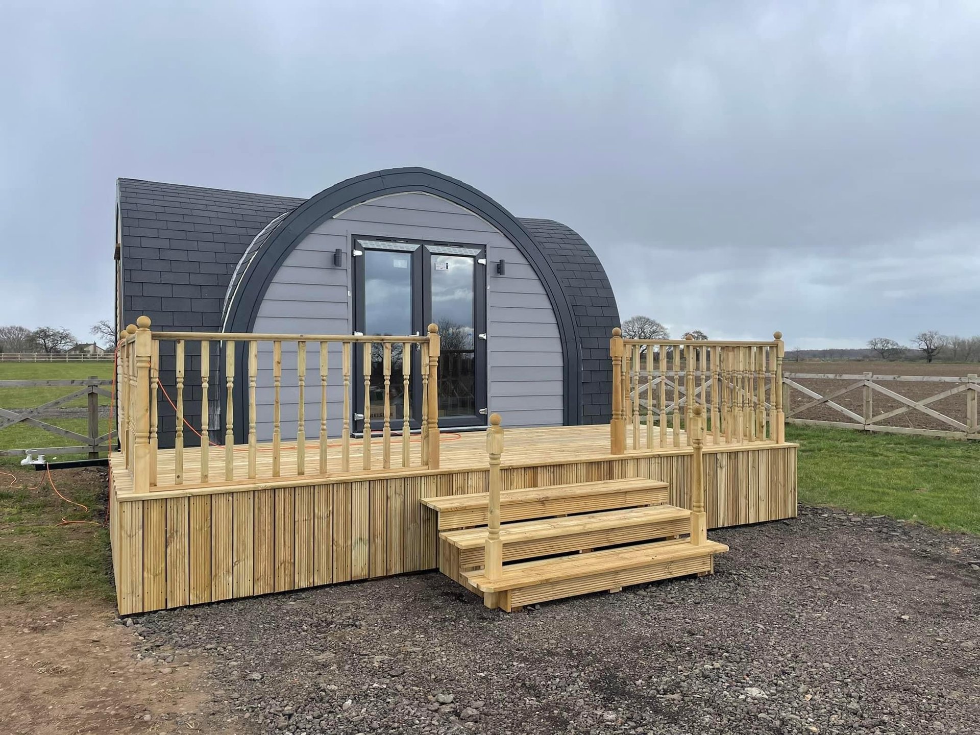 Glamping pod with curved roof, wooden deck, railings and steps in rural field setting