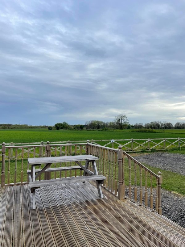 Wooden decking with picnic table and railing, overlooking green fields and distant trees