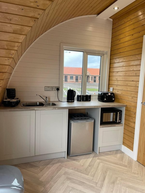 Compact kitchenette with white cabinetry, dishwasher, microwave and windows overlooking countryside