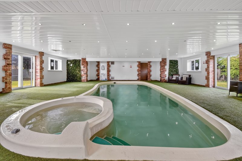 Indoor swimming pool with hot tub, artificial grass, brick pillars, and glass doors to grounds