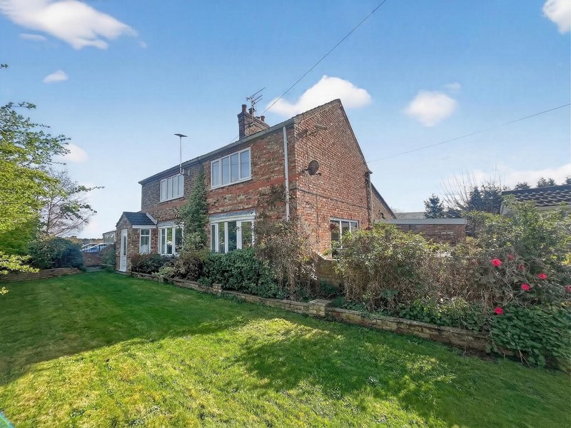 Brick semi-detached house with garden, viewed from lawn on sunny day