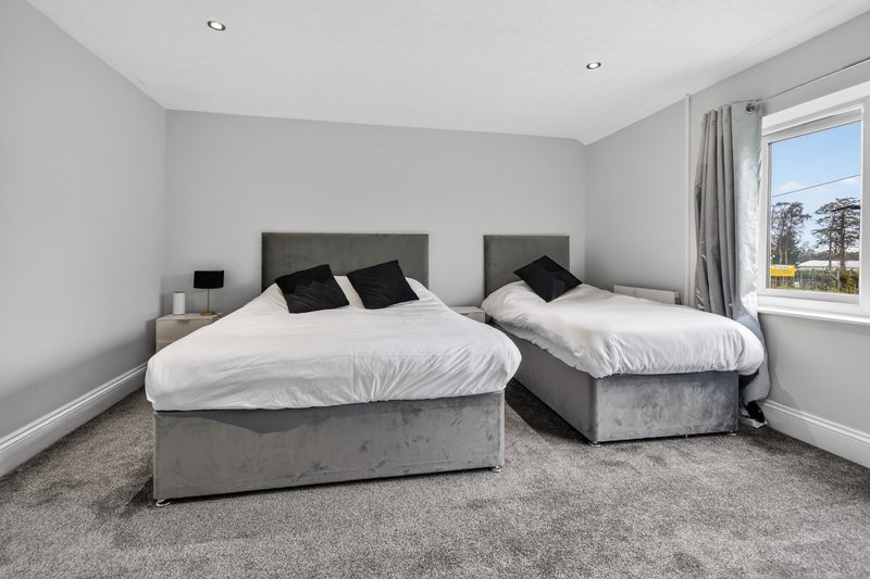 Bright bedroom with two grey upholstered beds, white bedding, black pillows, and large window with garden view