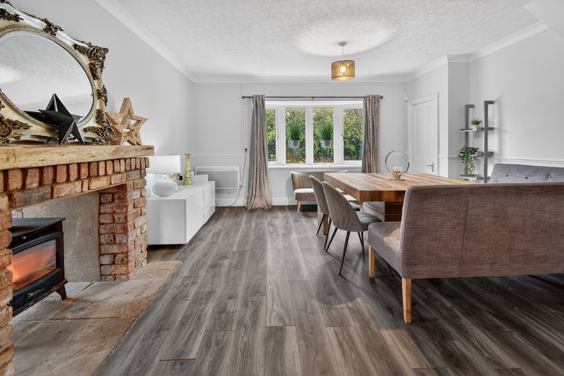 Open-plan living room with brick fireplace, wooden dining table, chairs and grey vinyl flooring