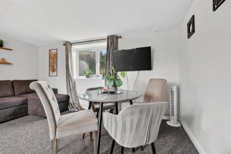 Modern living room with dining table, upholstered chairs, sofa, wall-mounted TV and window