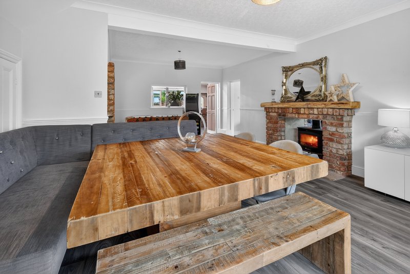 Open-plan living room with wooden dining table, grey sofa, brick fireplace and stove
