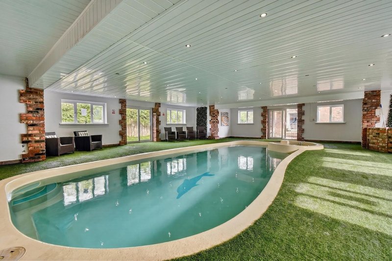 Indoor swimming pool with artificial turf surround, brick features, and multiple windows