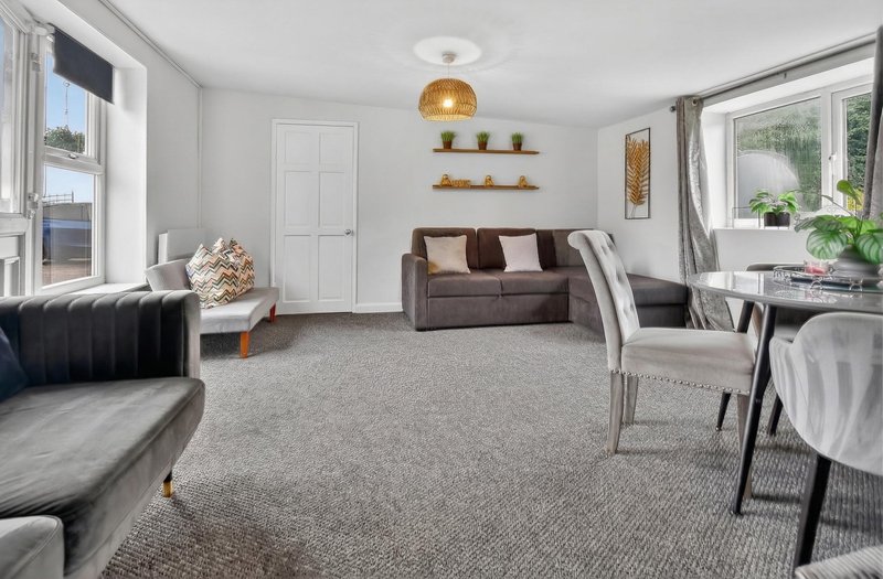 Spacious living room with gray carpet, multiple seating areas, pendant lighting, and large windows