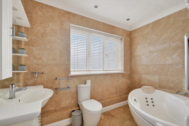 Bathroom with beige tile walls, white suite, bathtub, sink and window with shutters
