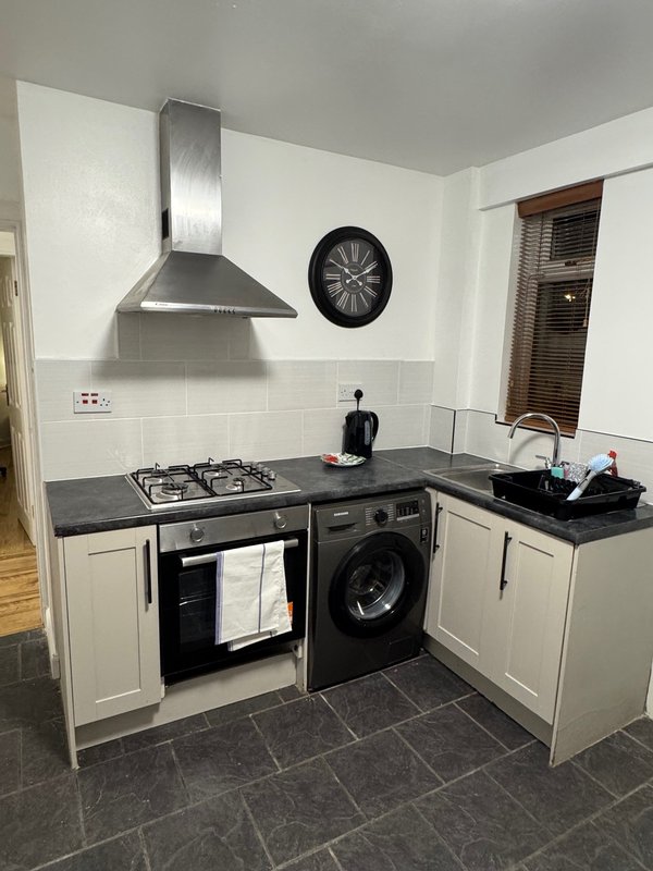 Modern kitchen with white cabinets, black countertop, gas hob, oven, washing machine and wall clock