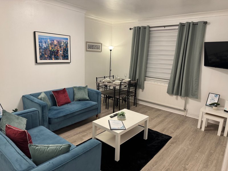 Modern living room with blue sofa, white coffee table, dining area and wall-mounted TV