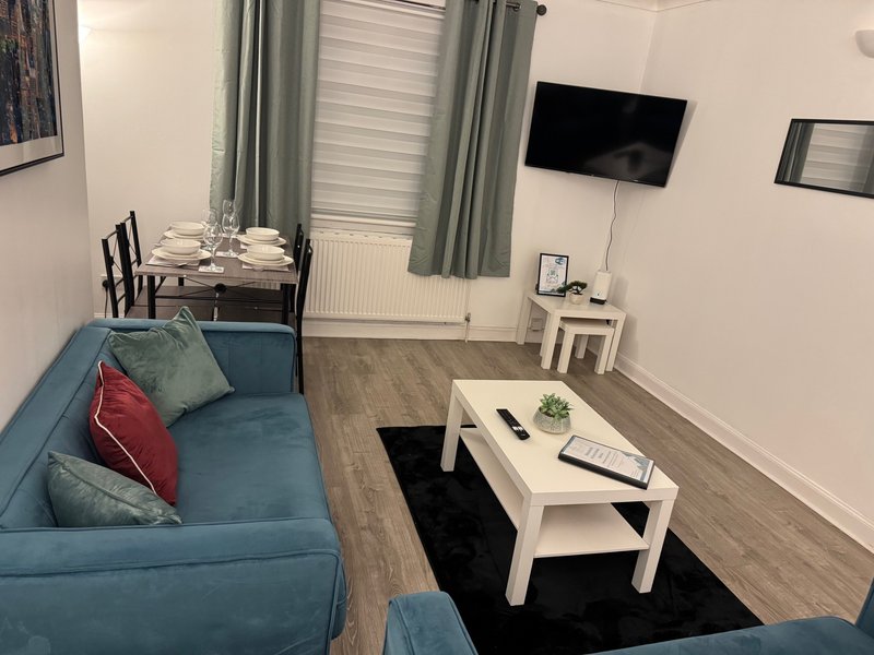 Open-plan living room with blue sofa, white coffee table, dining area and mounted TV