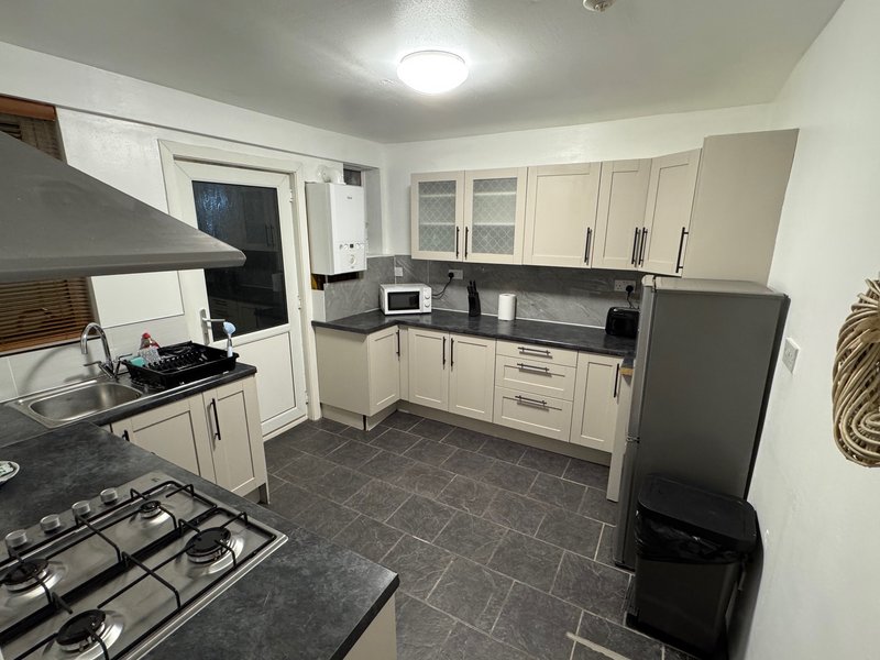 Modern kitchen with cream cabinets, black countertops, gas hob, microwave and stainless steel fridge