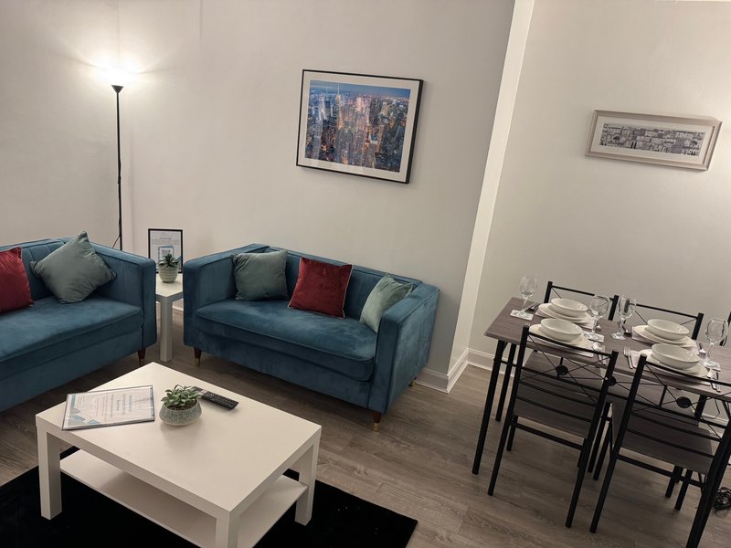 Living room with blue sofa, white coffee table, dining area, floor lamp and wall art