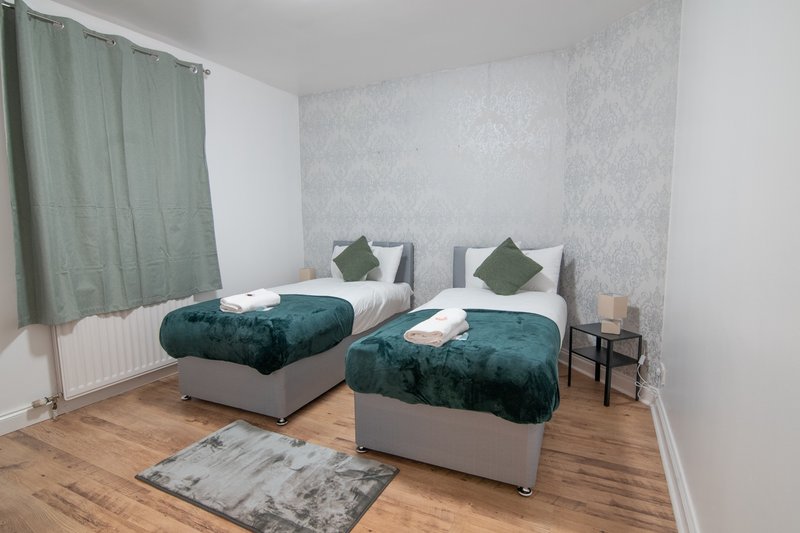 Twin bedroom with two beds, teal bedding, green curtains and wooden flooring