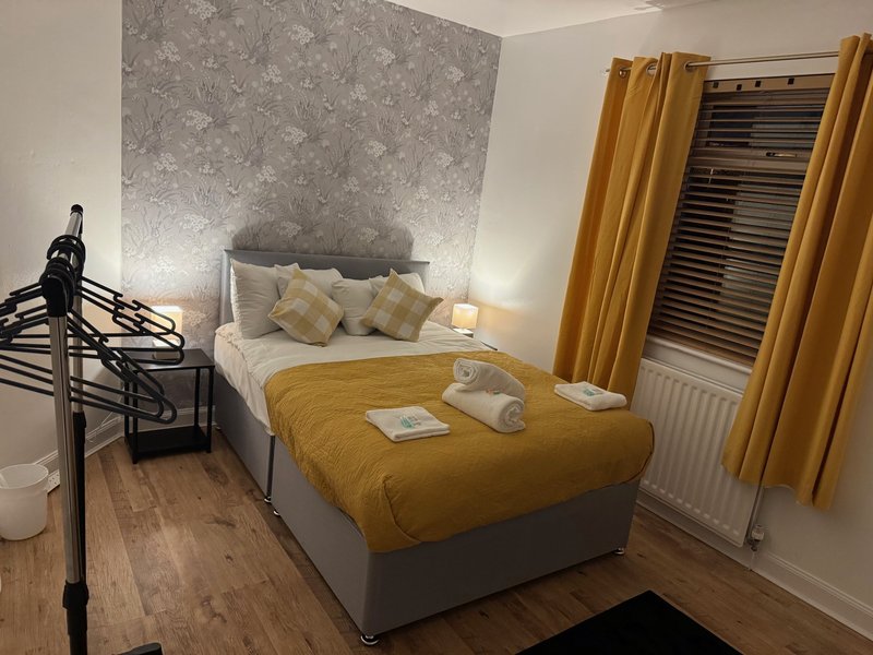 Bedroom with double bed, mustard-yellow bedding, patterned headboard, and golden curtains