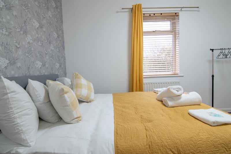 Bright bedroom with double bed, yellow bedding, white pillows and modern curtains