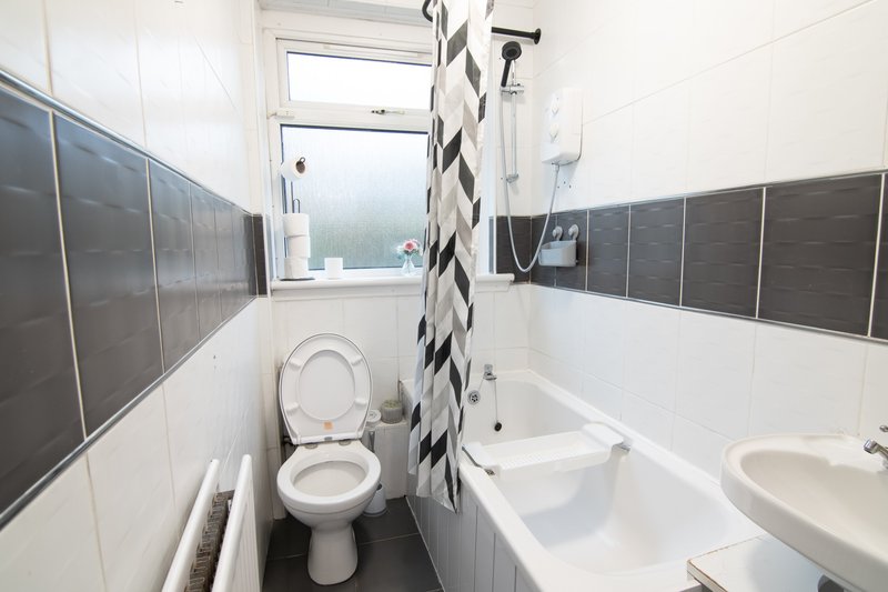 Modern bathroom with toilet, bathtub, sink, window and black tile accents