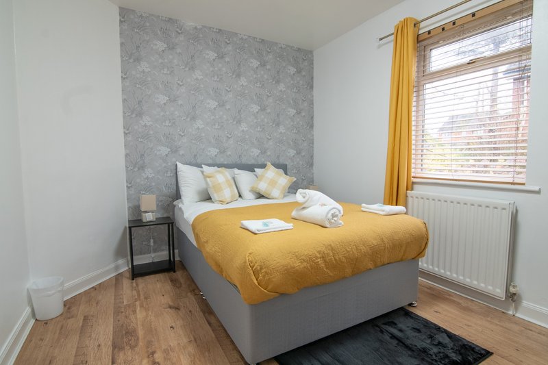 Bright bedroom with double bed, yellow bedding, grey headboard wall, and wooden flooring