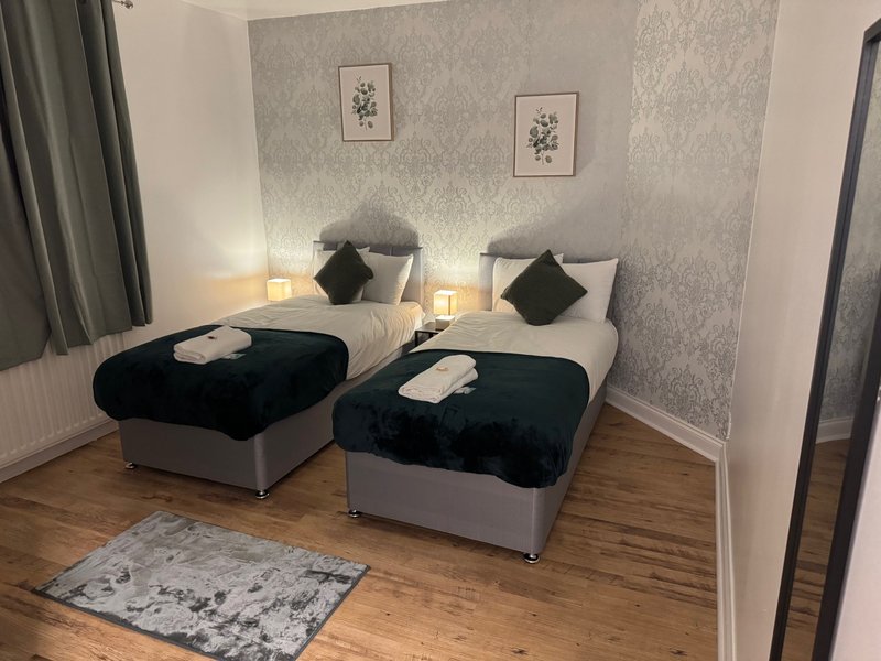 Twin bedroom with two single beds, black throws, cushions, bedside lamps and framed wall art