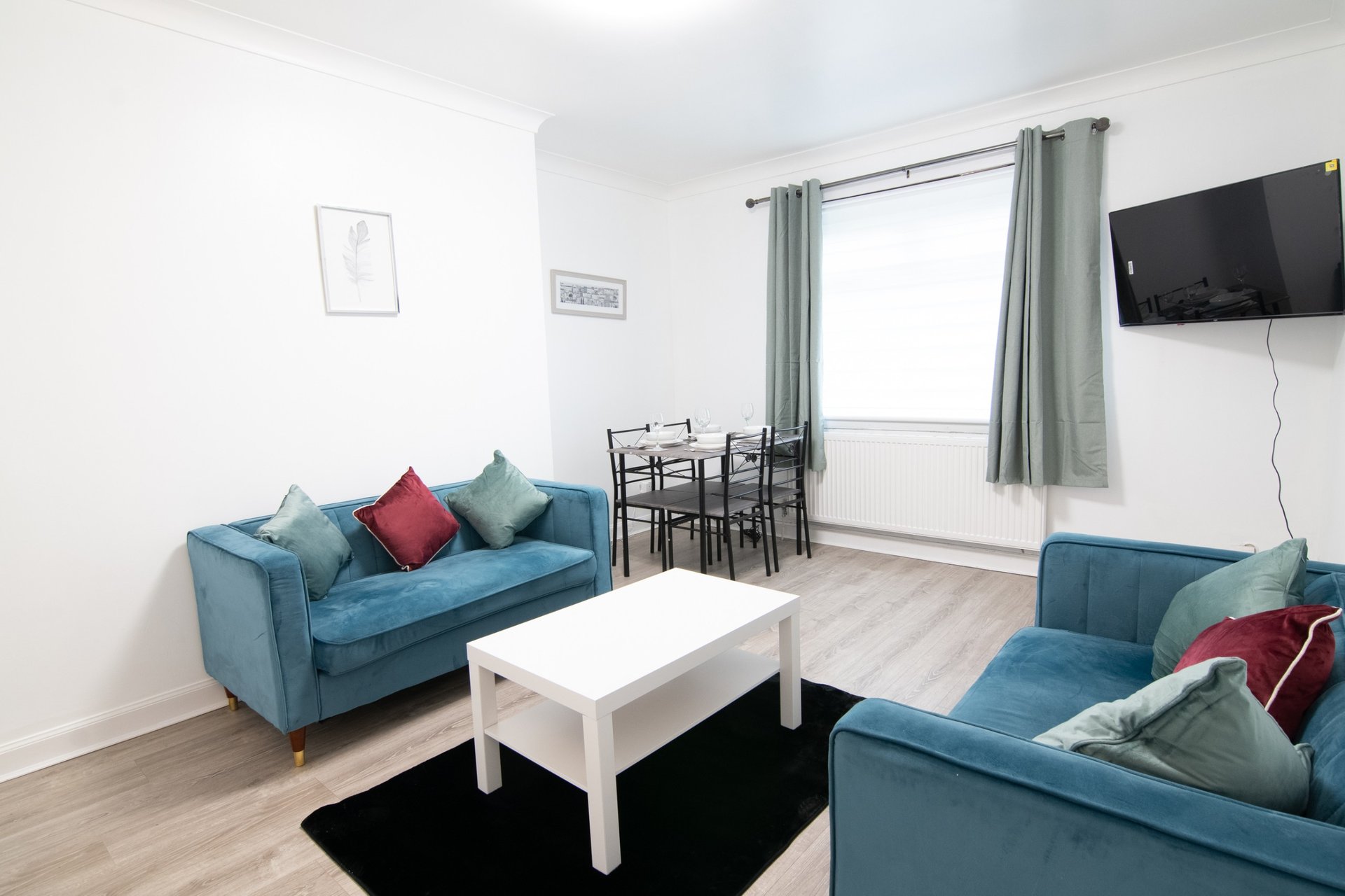 Bright living room with two blue sofas, white coffee table, dining chairs and wall-mounted TV