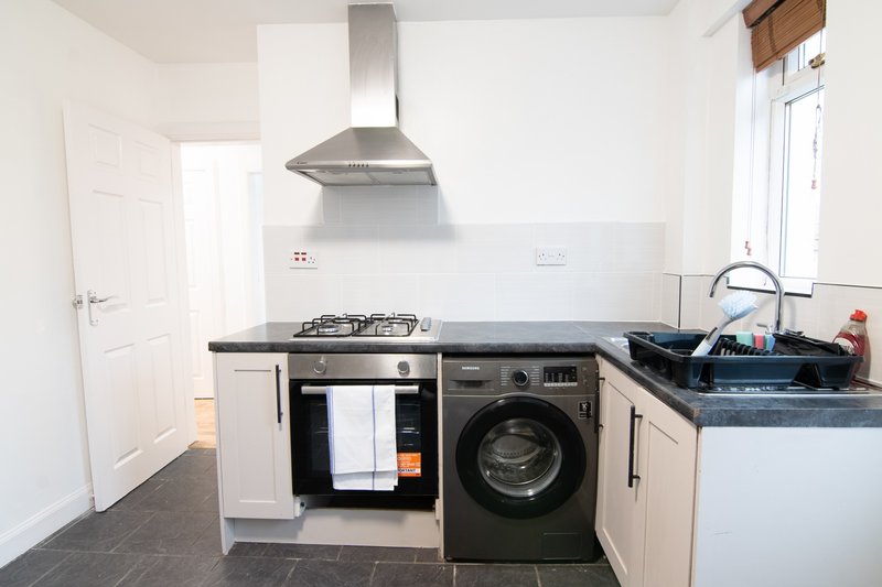 Modern kitchen with white cabinets, black countertop, gas hob, range hood, washing machine and sink