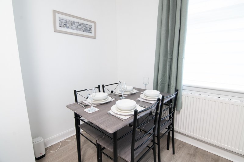 Dining area with black table, four chairs, place settings, and green curtains