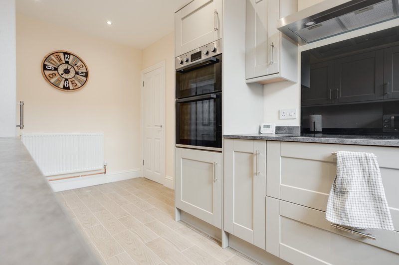 Modern kitchen with white cabinetry, black countertop, built-in oven and clock on wall