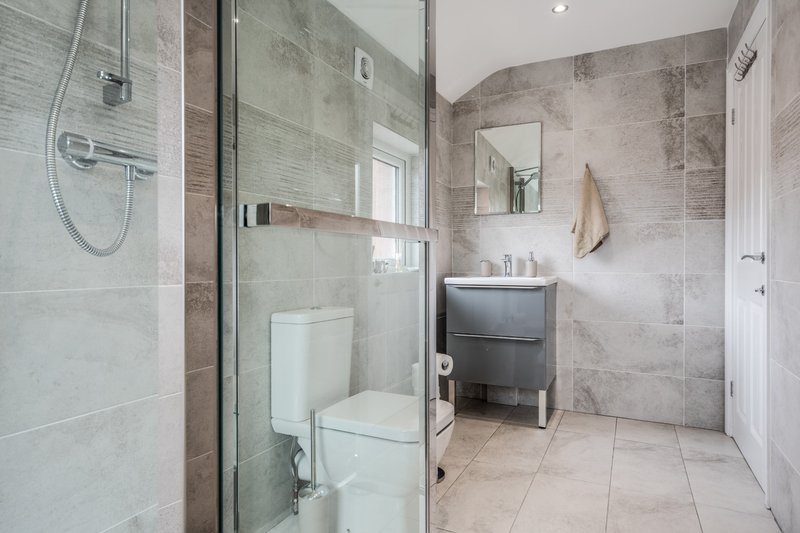 Modern bathroom with walk-in shower, toilet, vanity sink, mirror and tiled flooring