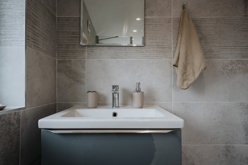 Modern bathroom with white sink, dark vanity, mirror and towel rail