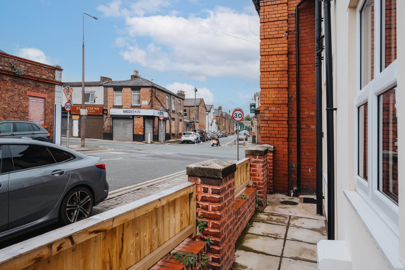 Street view of brick terraced house with driveway, parked car and neighboring buildings