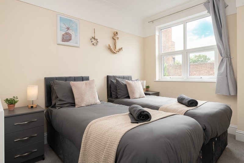 Bright bedroom with two single beds, grey bedding, wooden nightstand and window with garden view