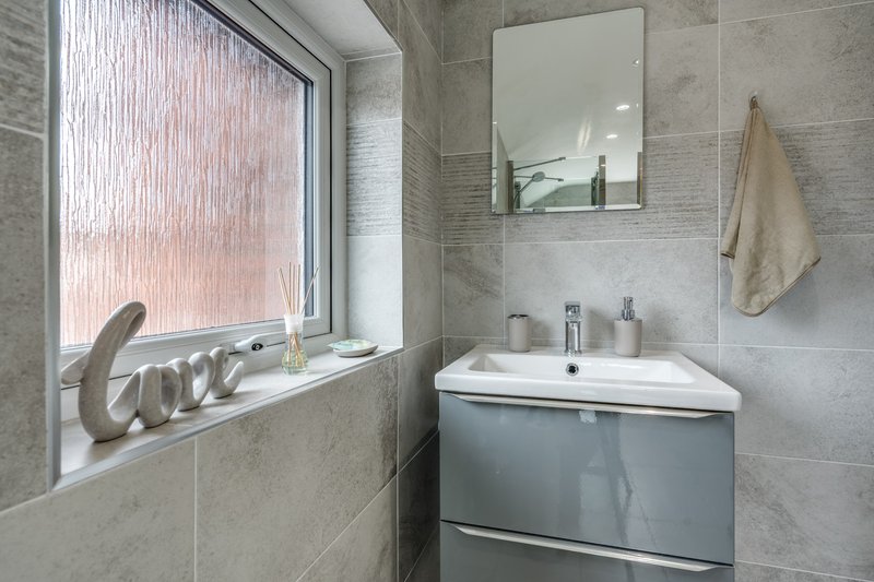 Modern bathroom with grey tile walls, white sink, mirror, and window with textured glass