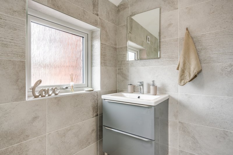 Modern bathroom with gray vanity unit, mirror, window and beige tile walls