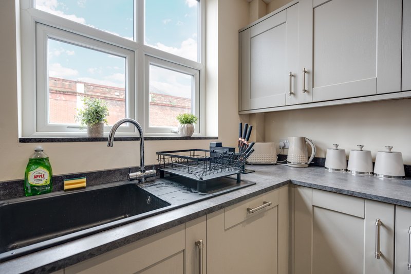 Modern kitchen with cream cabinetry, black countertop, sink and window overlooking brick building