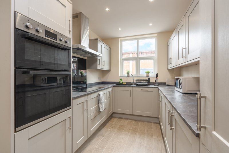 Modern kitchen with cream cabinetry, black built-in appliances, dark countertops and wooden flooring