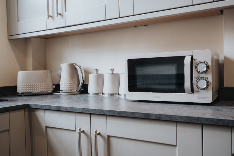 Modern kitchen countertop with white microwave, kettle, toaster and kitchen accessories