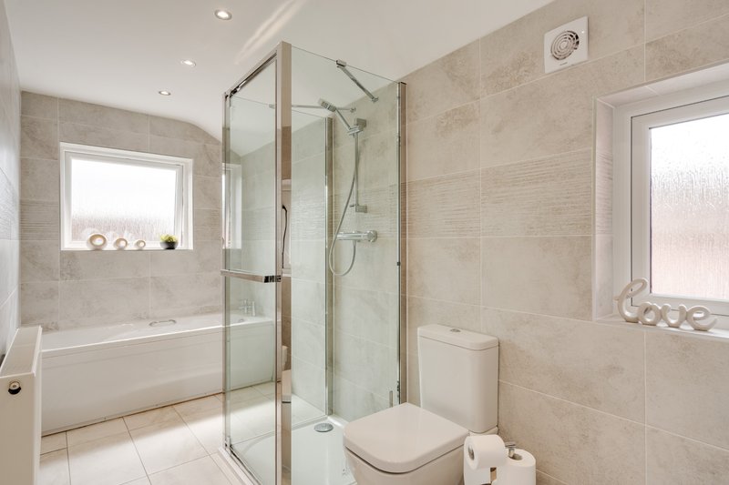 Modern bathroom with walk-in shower, white toilet, bathtub and tiled walls