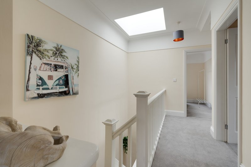 Bright hallway with skylight, wooden banister, wall art, and access to multiple rooms