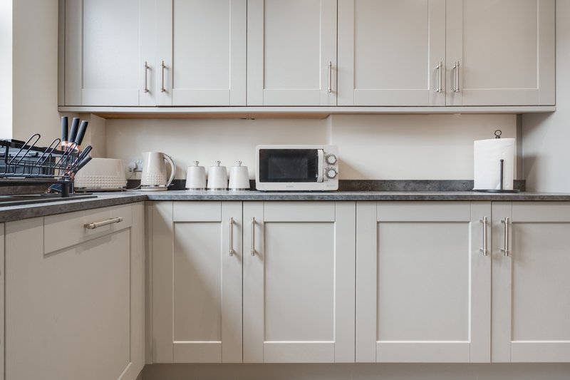 Modern kitchen with white cabinetry, gray countertop, microwave, and appliances