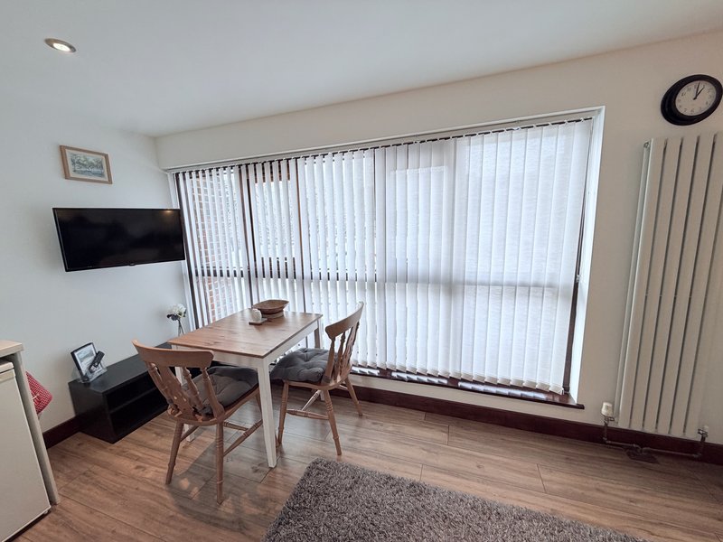 Bright living room with wooden desk, chair, wall-mounted TV, and vertical blinds covering large window
