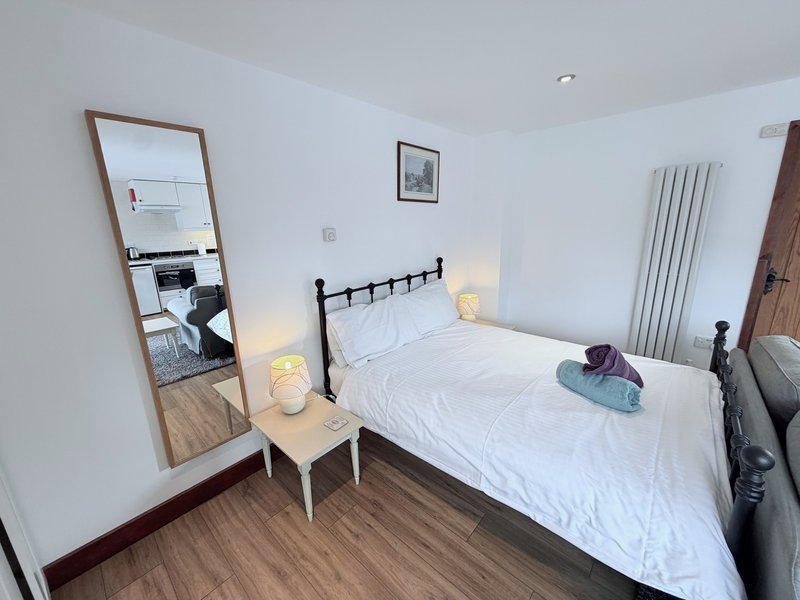 Bedroom with double bed, black headboard, wooden flooring, full-length mirror and bedside lamp